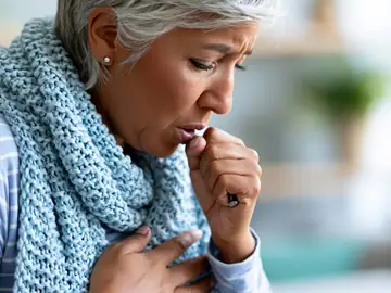 Senior woman coughing and holding her chest, showing flu and respiratory infection symptoms treated at Memorial Heights Emergency Center in Houston, TX