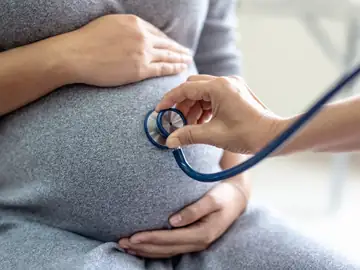 Healthcare professional performing a prenatal checkup with a stethoscope on a pregnant woman’s belly at Memorial Heights Emergency Center in Houston, TX
