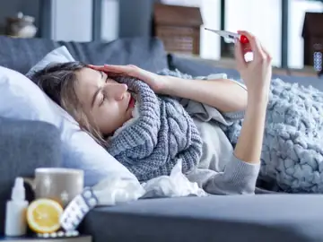 Woman with fever resting on a couch while checking her temperature, illustrating RSV and respiratory illness symptoms treated at Memorial Heights Emergency Center in Houston, TX